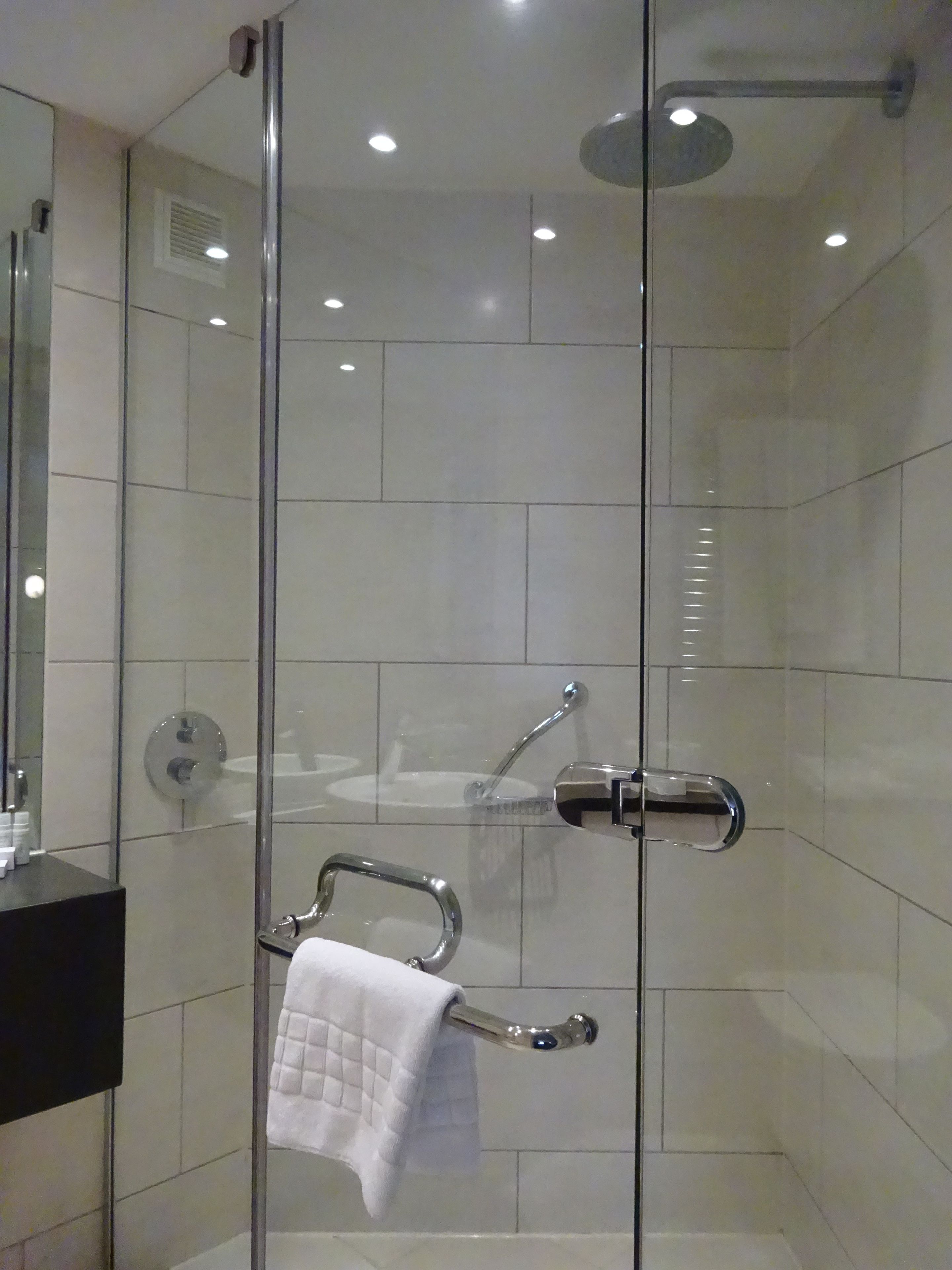Ein modernes Badezimmer mit einer Duschkabine aus Glas, einem schwarzen Waschtisch und einem Handtuchhalter mit einem weißen Handtuch.