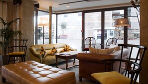 Una sala de estar moderna con un sofá, sillas y una mesa de centro. Amplias ventanas ofrecen vistas a la calle.