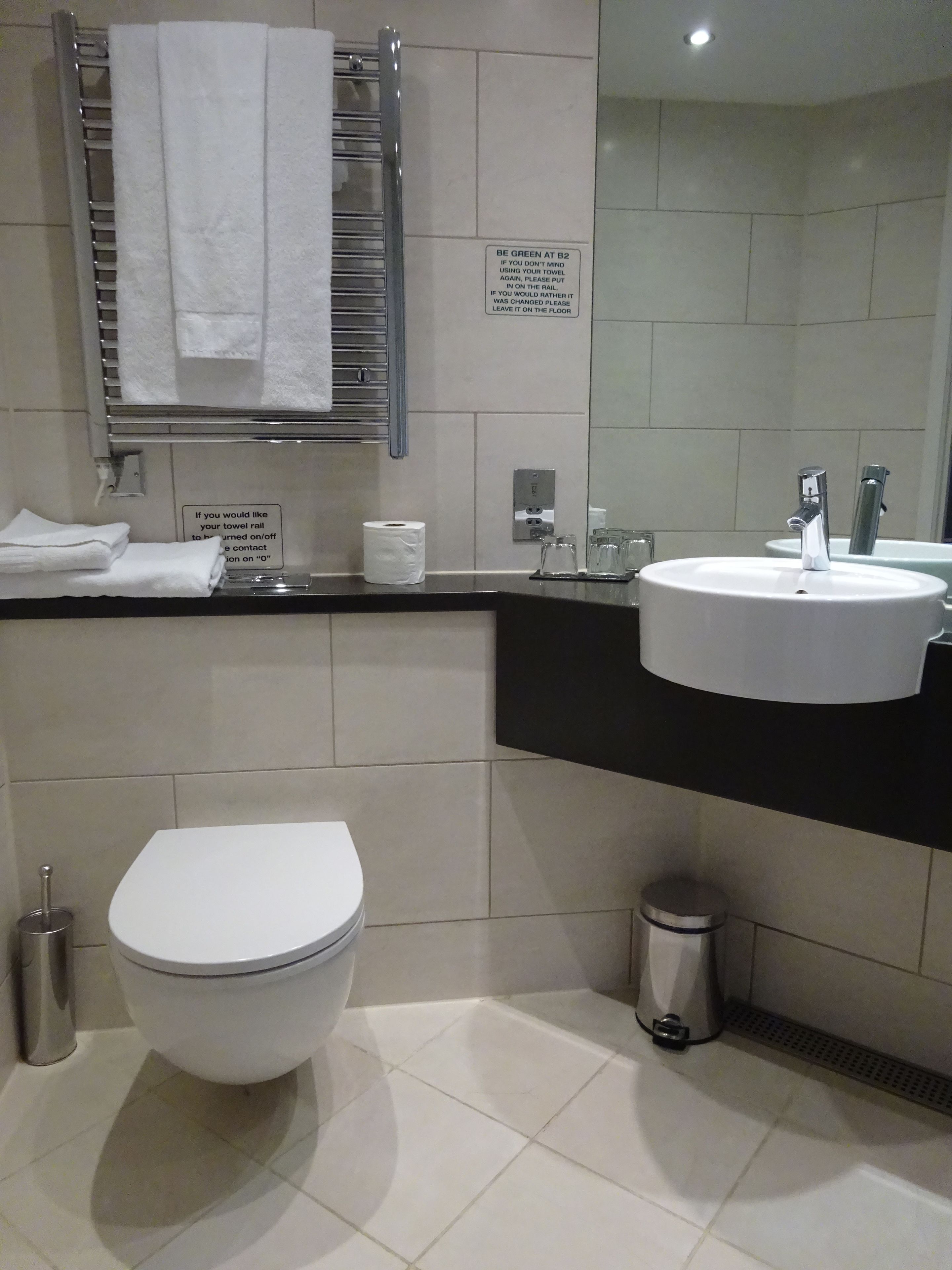 Un bagno moderno con servizi igienici, lavandino e porta asciugamani. Sono presenti indicazioni sull'uso degli asciugamani e un cestino.