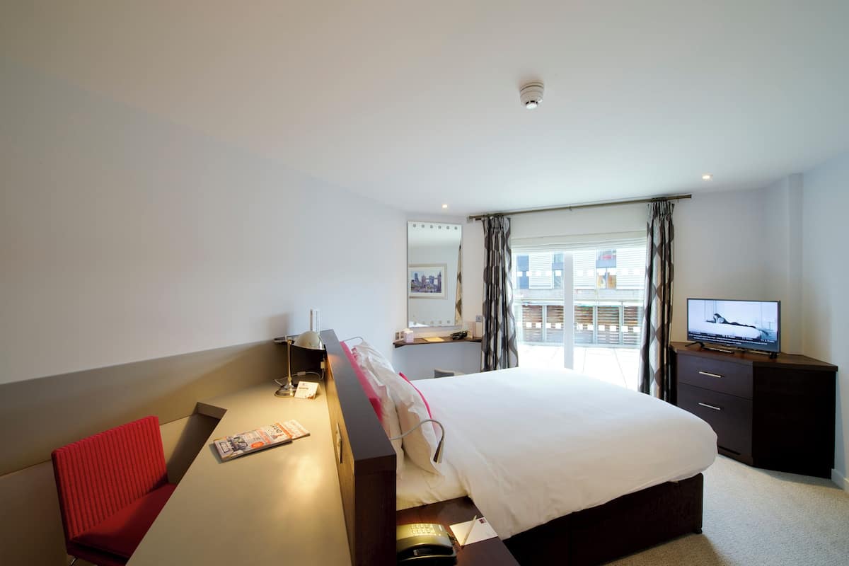 Une chambre d’hôtel équipée d’un lit, d’un bureau, d’une chaise, d’une télévision et d’une fenêtre avec des rideaux.