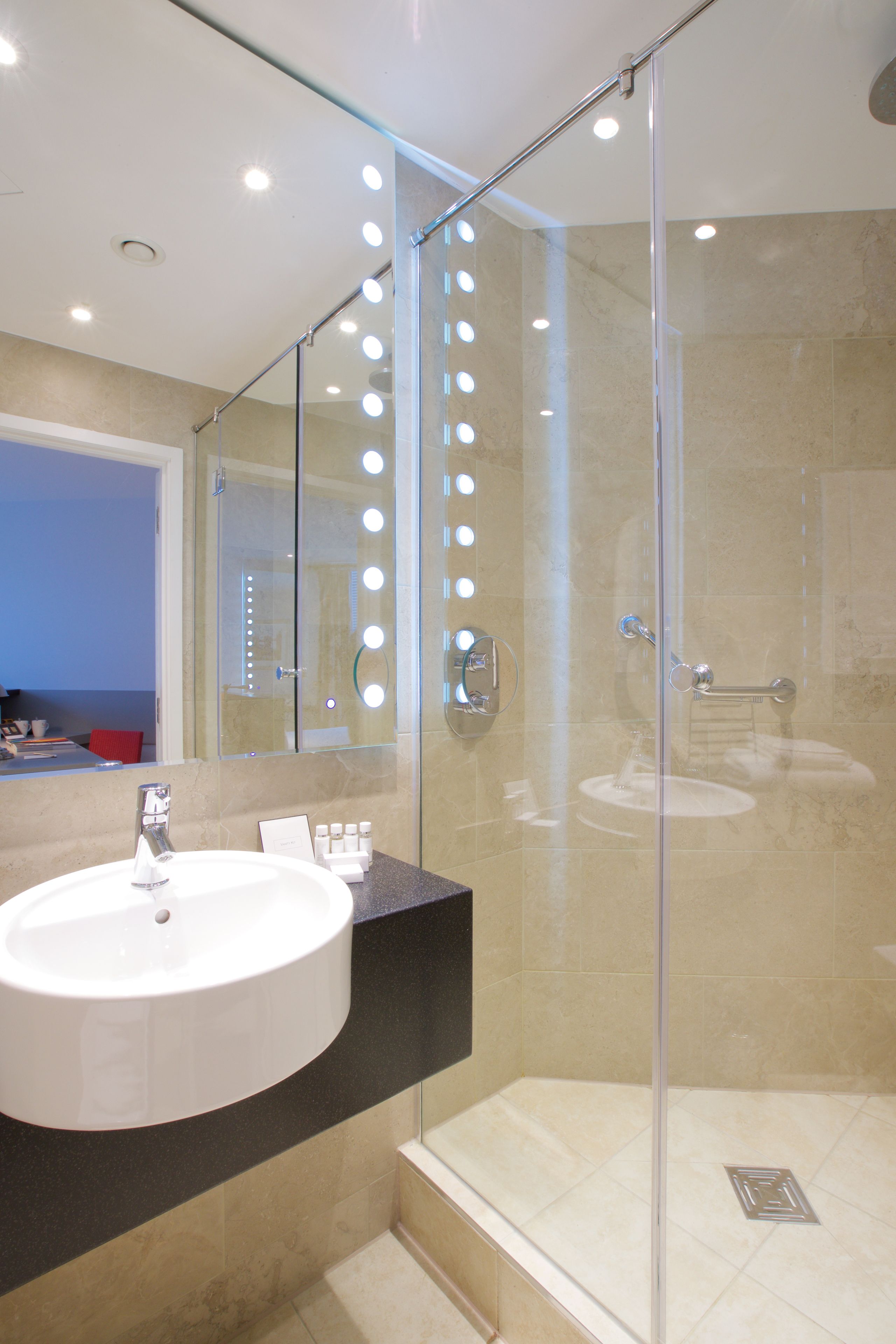 Un baño moderno con ducha envuelta en vidrio, un lavabo redondo y un mueble de tocador con espejo.