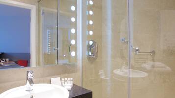 Un baño moderno con ducha envuelta en vidrio, un lavabo redondo y un mueble de tocador con espejo.