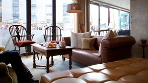 Ein gemütliches Wohnzimmer mit Ledersofa, Holzstühlen, einem Couchtisch und Blick auf die Stadt durch große Fenster.