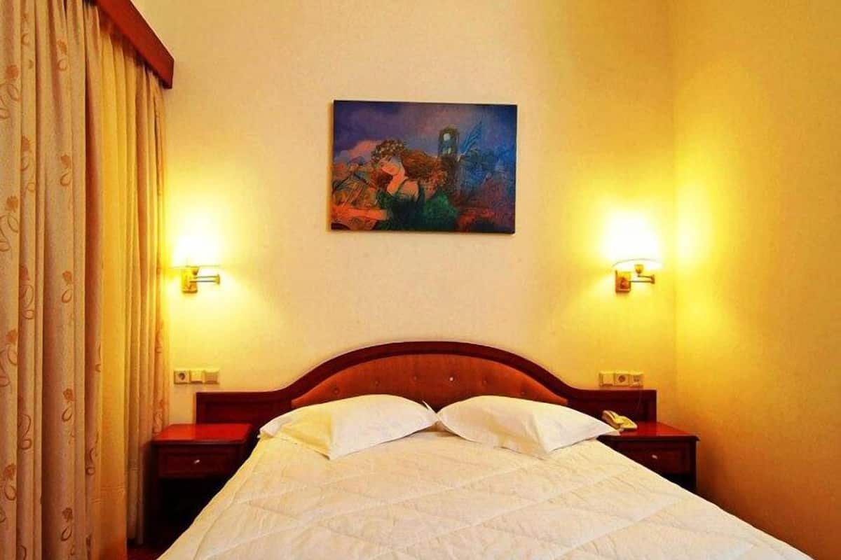 A hotel room with a bed, two bedside tables, a painting on the wall, and curtains.