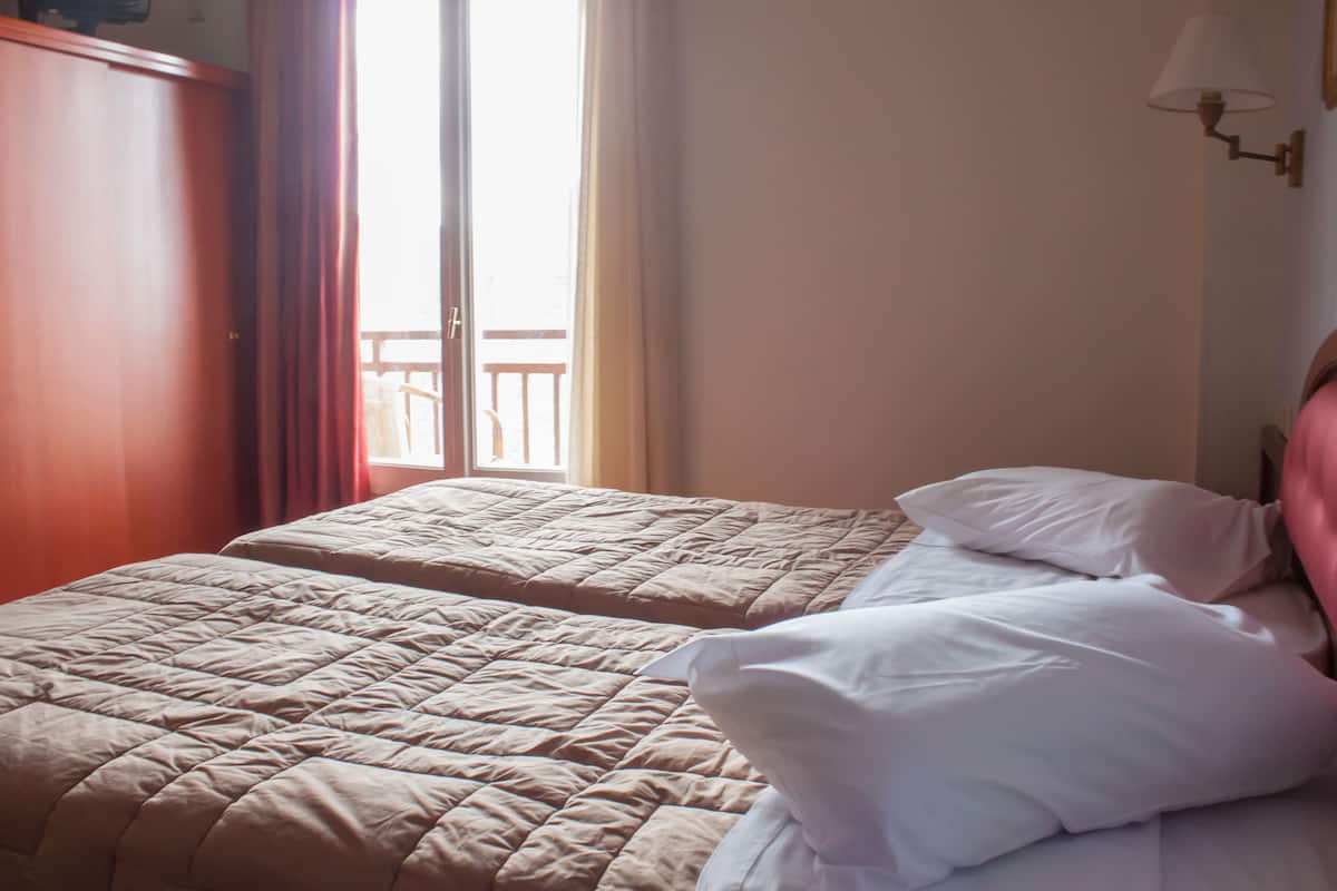 A room with two beds, a wardrobe, and a view of a balcony.