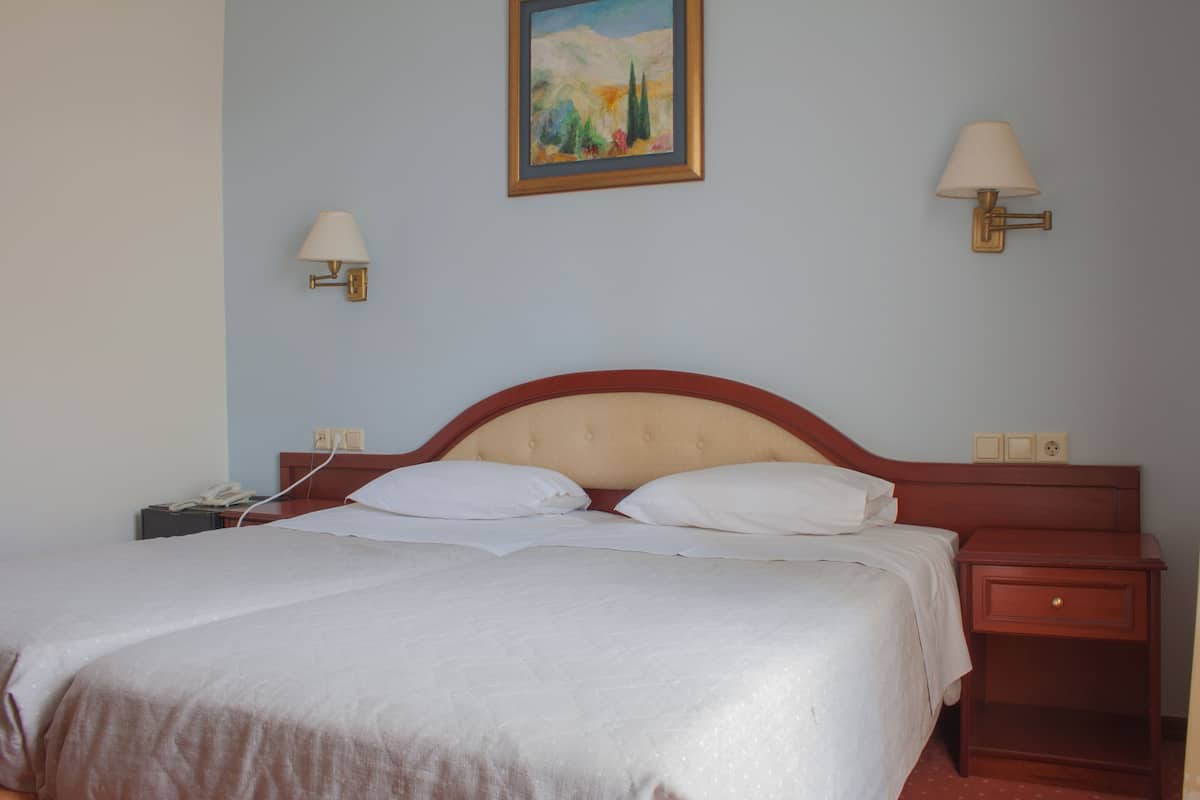 A neatly made bed with white linens, a wooden headboard, and two bedside lamps.