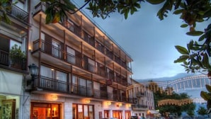 Un hotel de varios pisos con balcones, un restaurante en la planta baja y coches estacionados frente al edificio.