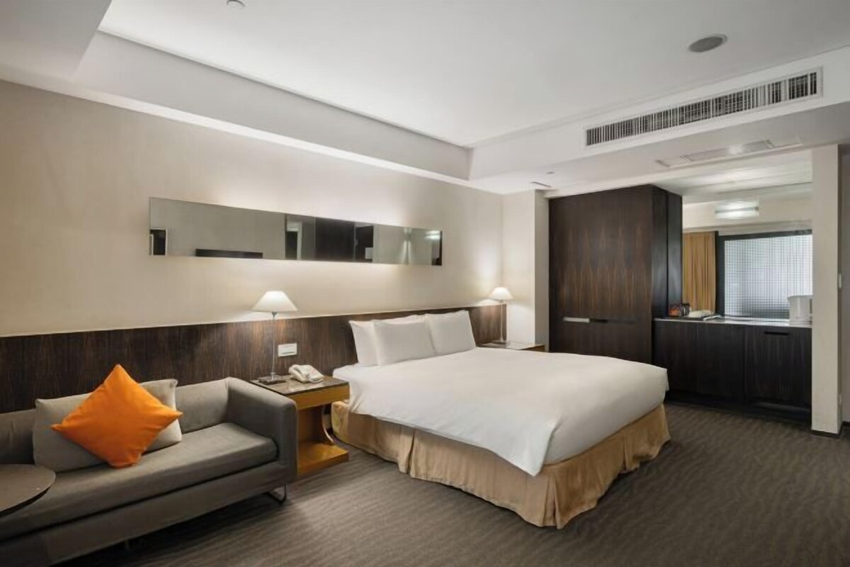 A hotel room with a bed, a sofa, a desk, and a mirror.