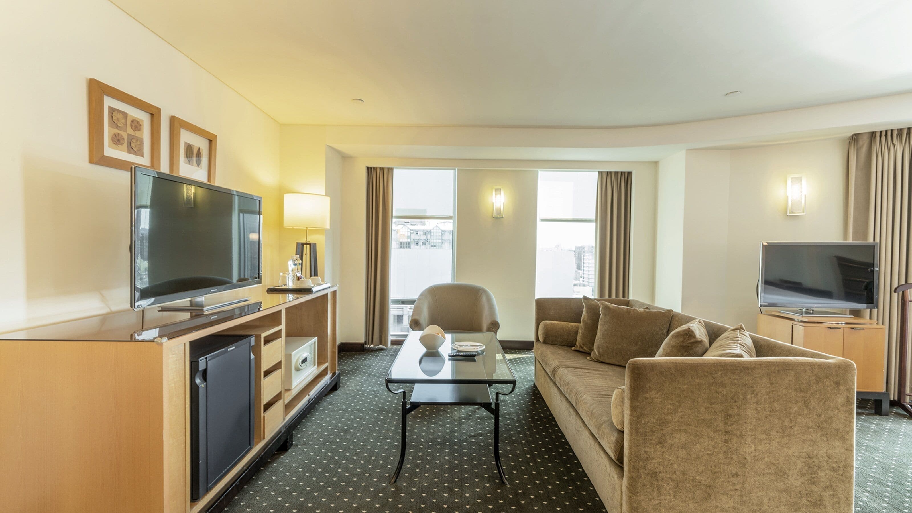 A hotel room with a flat-screen TV, a sofa, a coffee table, and a television on a stand.
