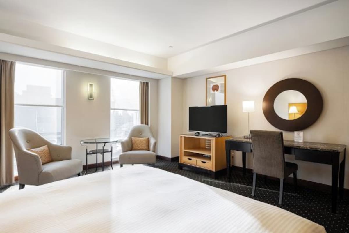 A hotel room with a large bed, two armchairs, a desk with a TV, and a mirror on the wall.