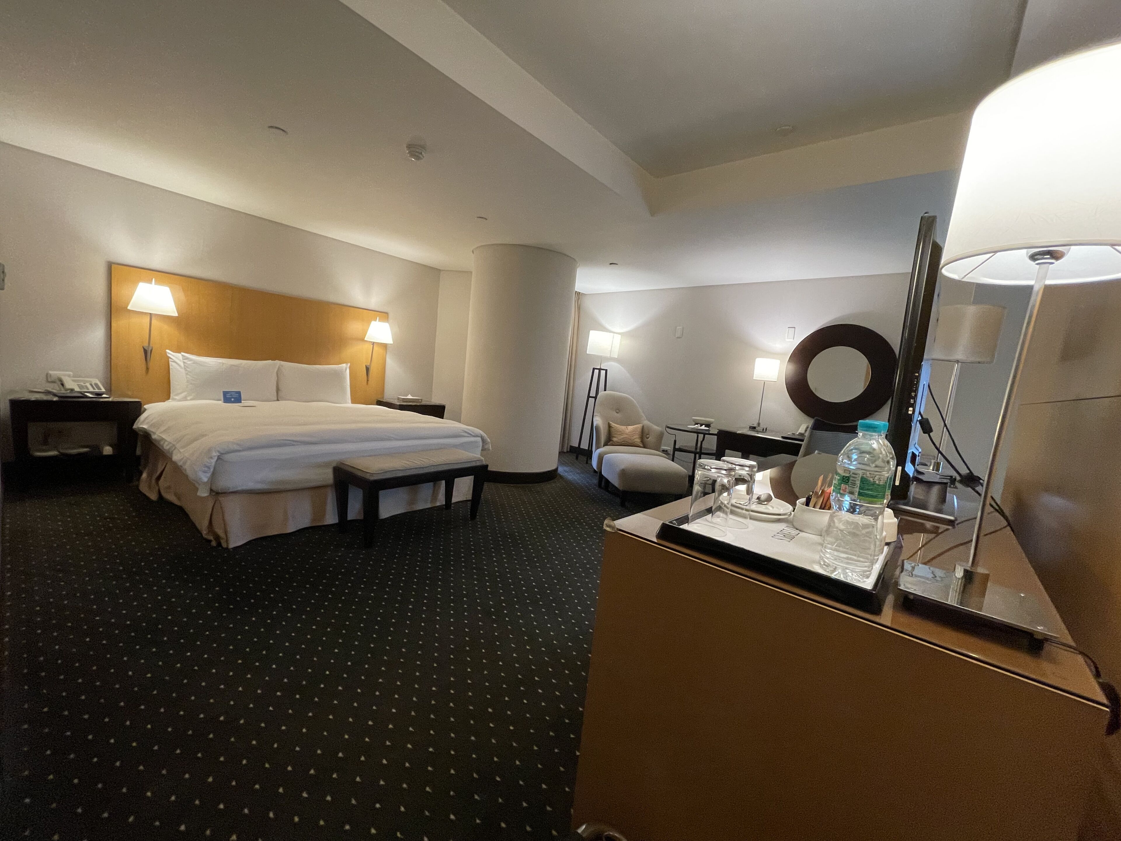 Habitación de hotel con cama, mesitas de noche, escritorio, silla, lámpara y espejo.