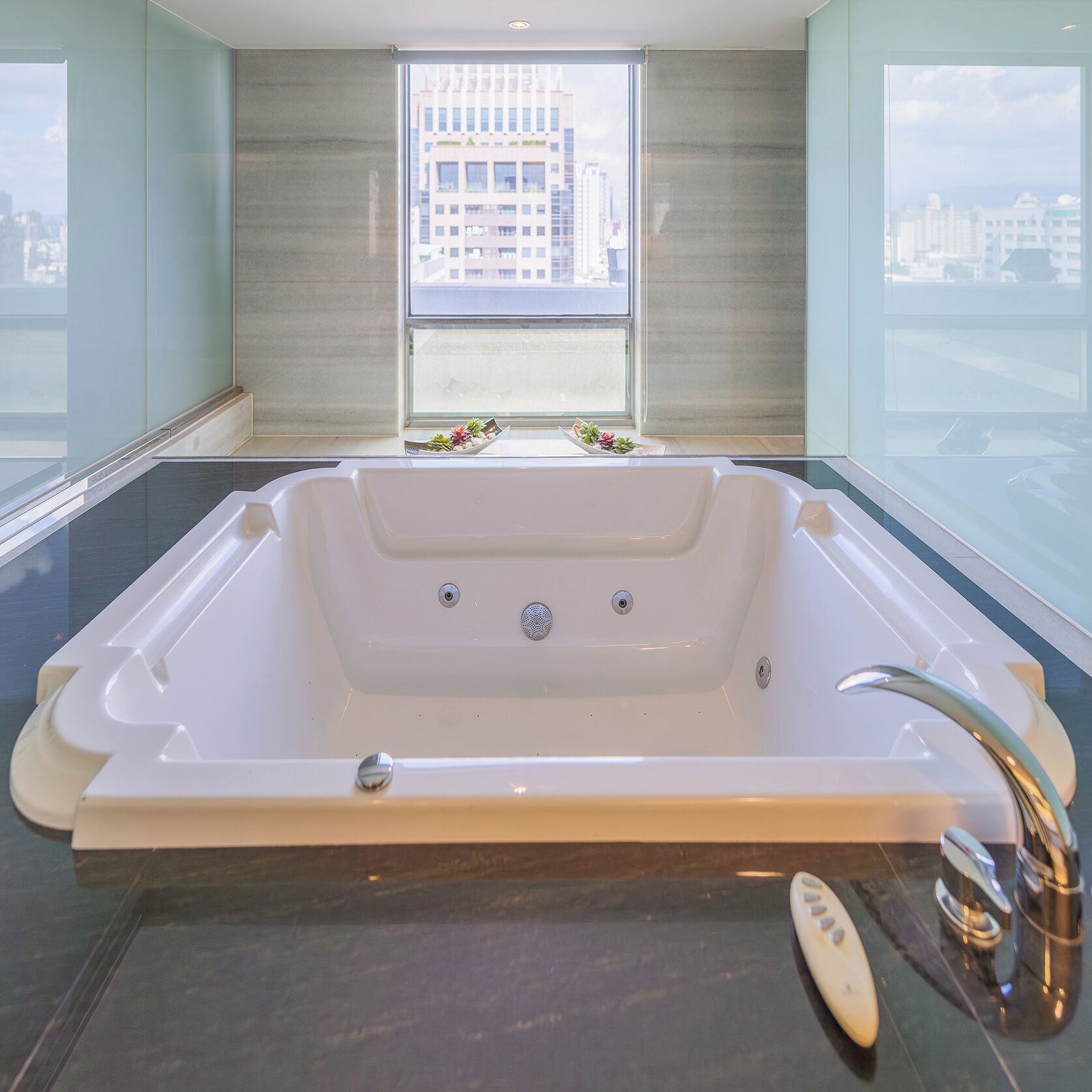 Un baño moderno con una bañera grande, un ventanal con vistas a la ciudad y un control remoto en el suelo.