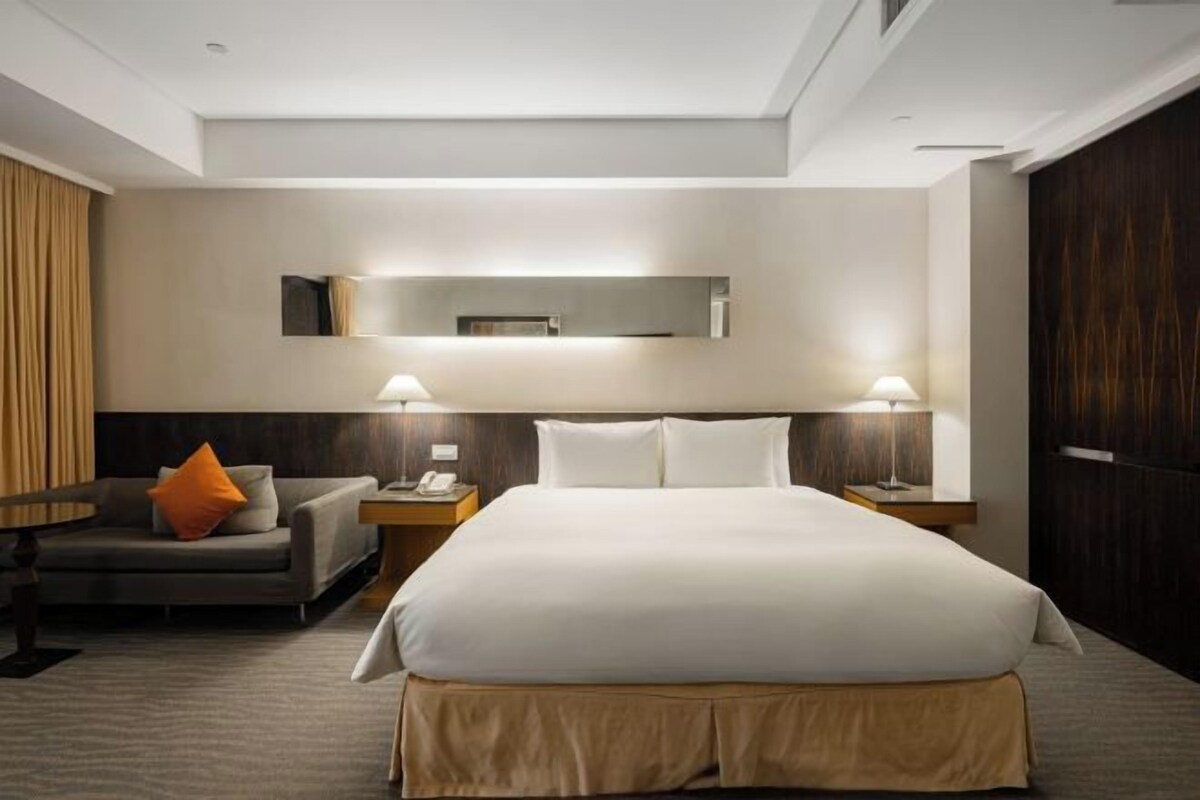 Habitación de hotel con una cama grande, dos mesitas de noche, un escritorio, una silla y un espejo en la pared.