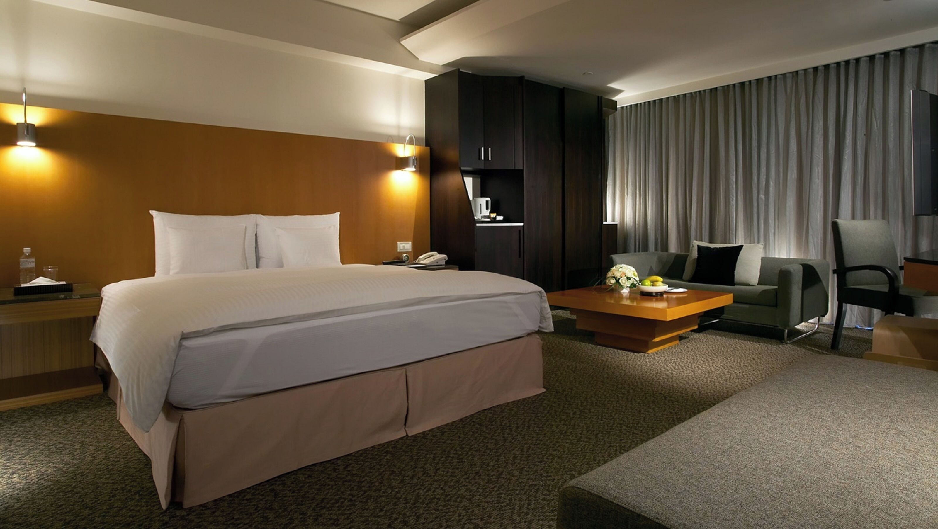 A hotel room with a large bed, a desk, a chair, and a sofa.