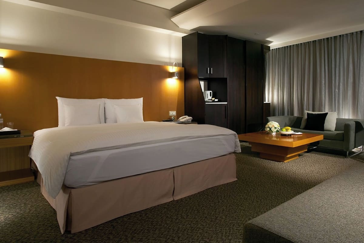 A hotel room with a large bed, a desk, a chair, and a sofa.