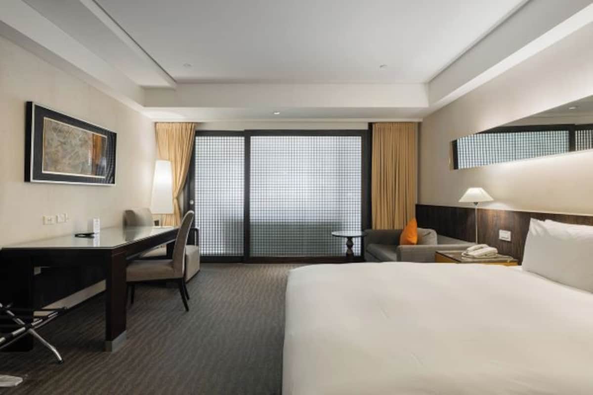 A hotel room with a bed, desk, chair, and a view through a large window.