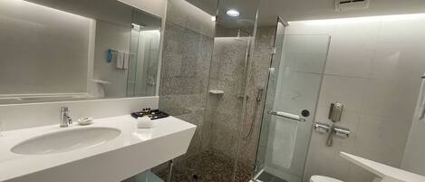 Un baño moderno con ducha envuelta en vidrio, un espejo grande y un lavabo blanco.