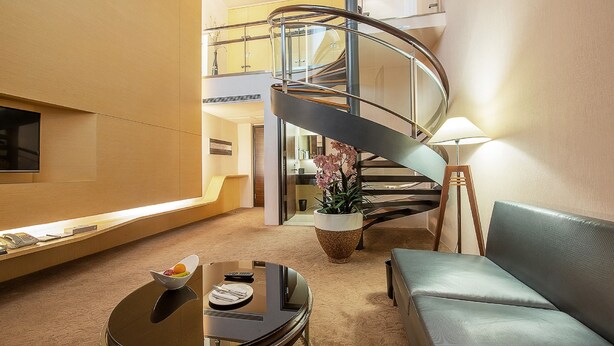 Un vestíbulo de hotel con una escalera de caracol, un sofá, una mesa de centro con un frutero y una lámpara.