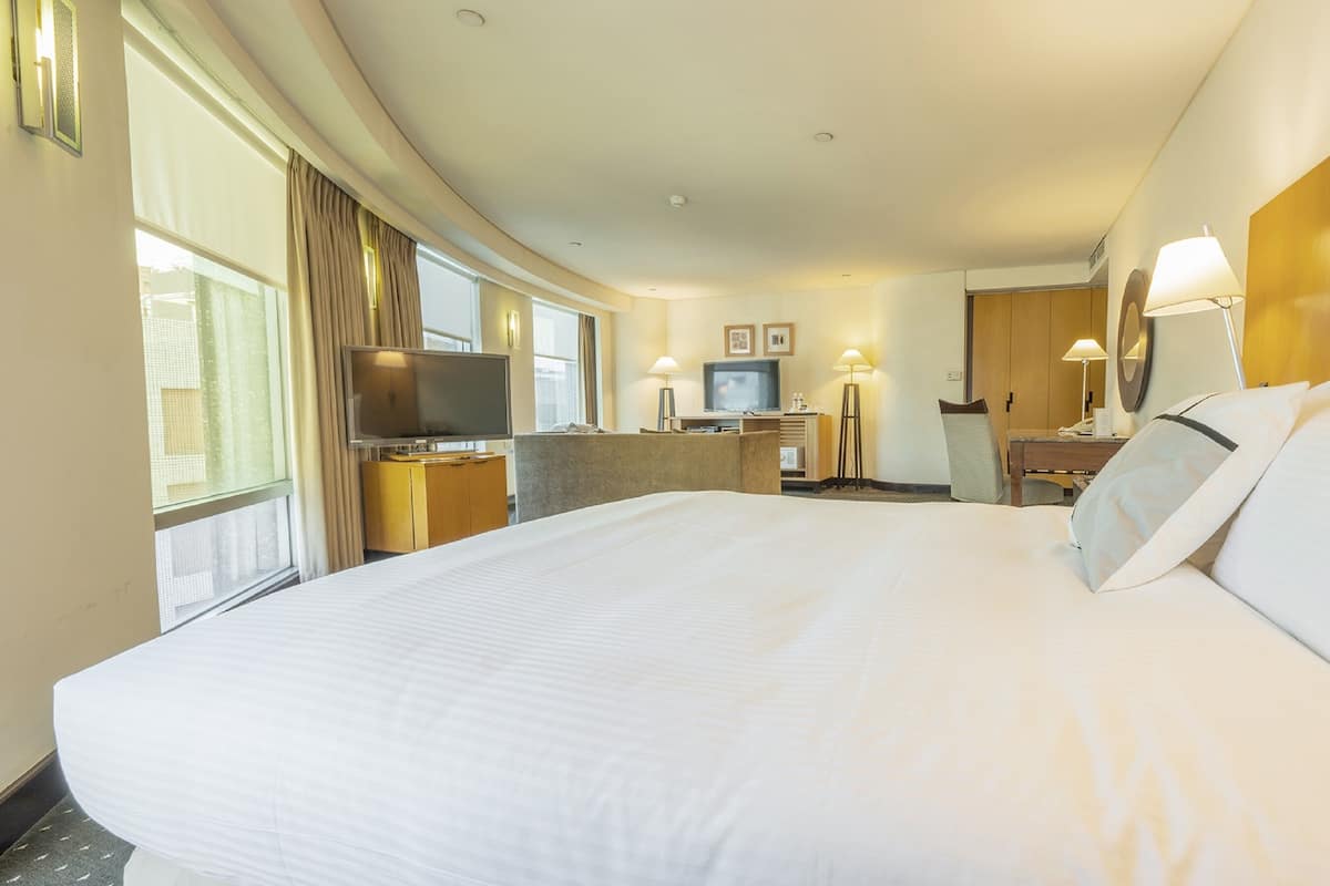 Quarto de hotel com uma cama grande, televisão, escrivaninha com computador e uma cadeira.