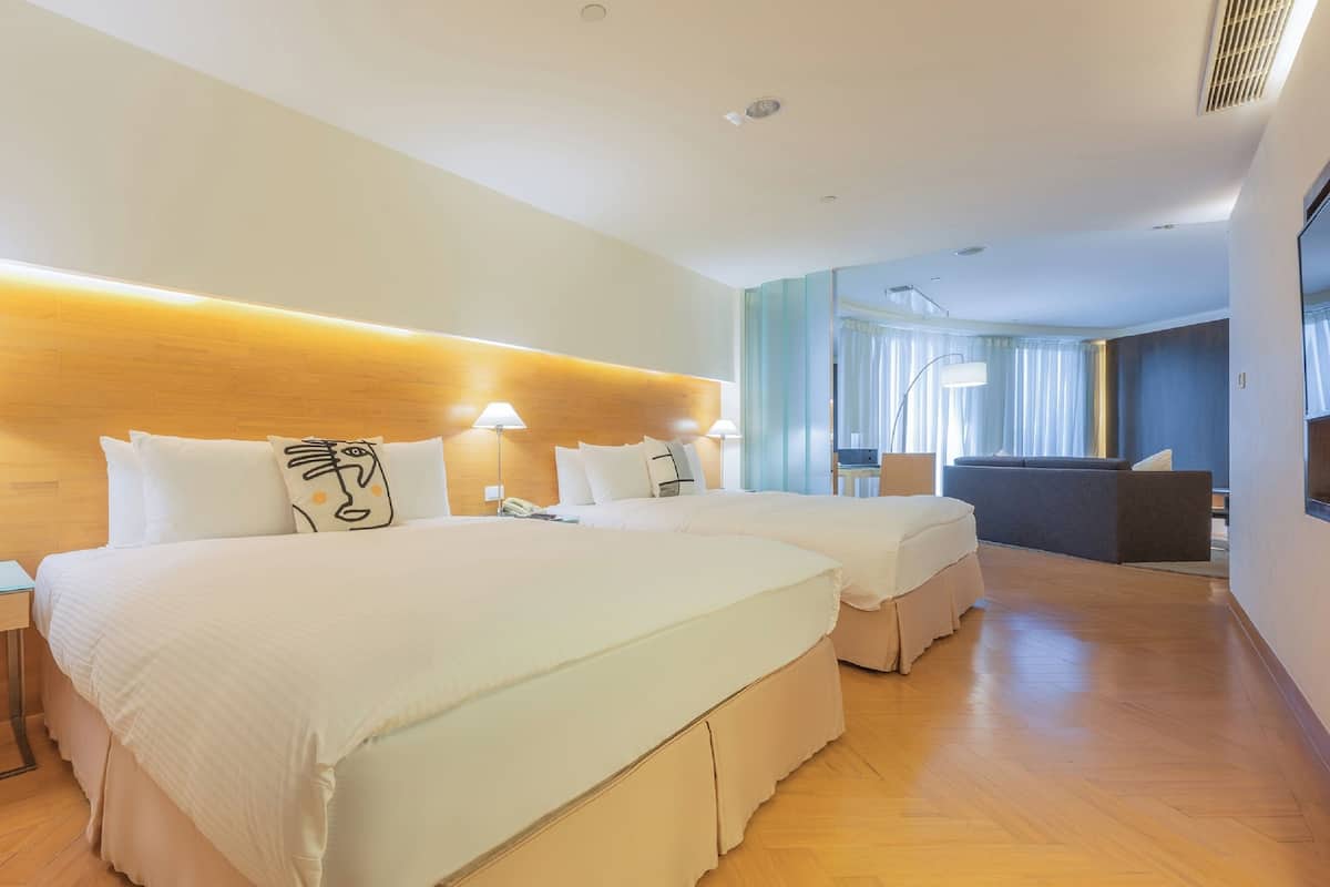 Quarto de hotel com duas camas, uma escrivaninha, uma cadeira e um sofá.