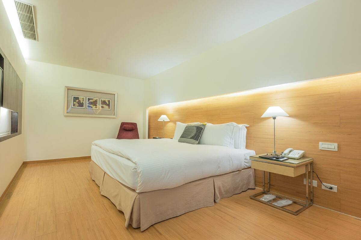 Quarto de hotel com cama, abajures, mesa de cabeceira, espelho e um quadro na parede.
