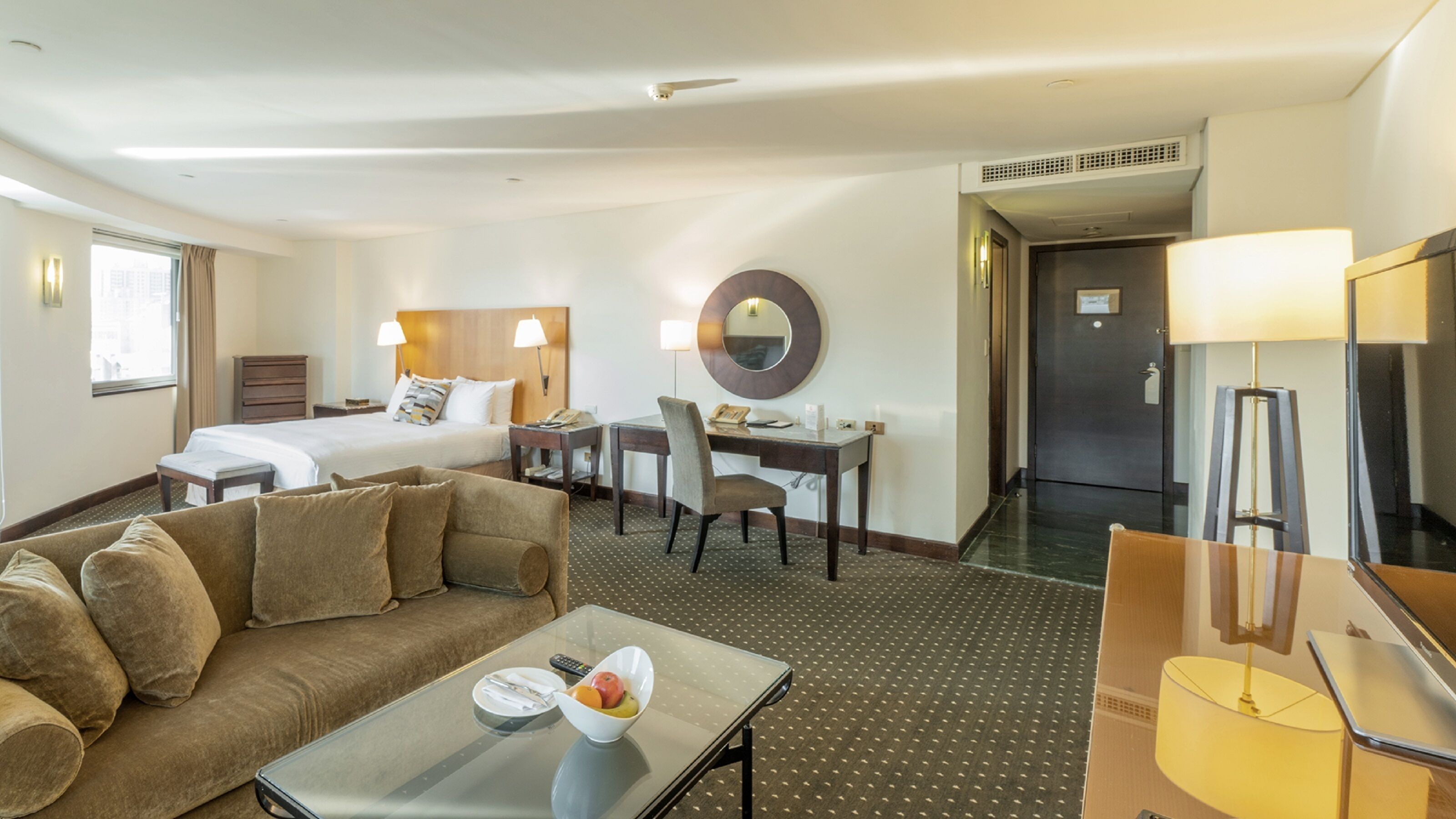A hotel room with a bed, a desk, a chair, a sofa, a coffee table, and a mirror.