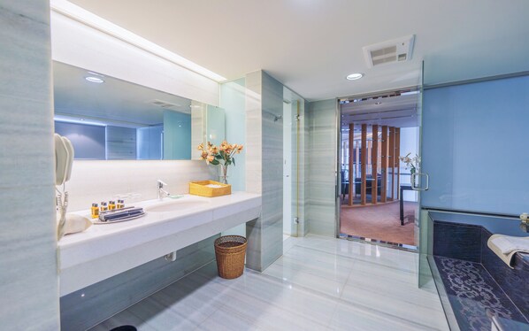 Un baño moderno con un espejo grande, lavamanos blanco y un separador de vidrio que da acceso a la zona de ducha.