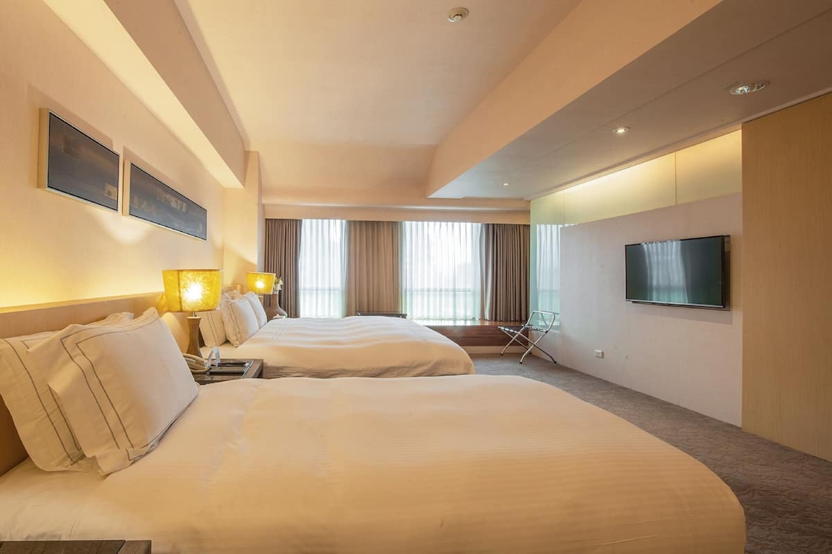 Quarto de hotel com duas camas, televisão e uma cadeira.
