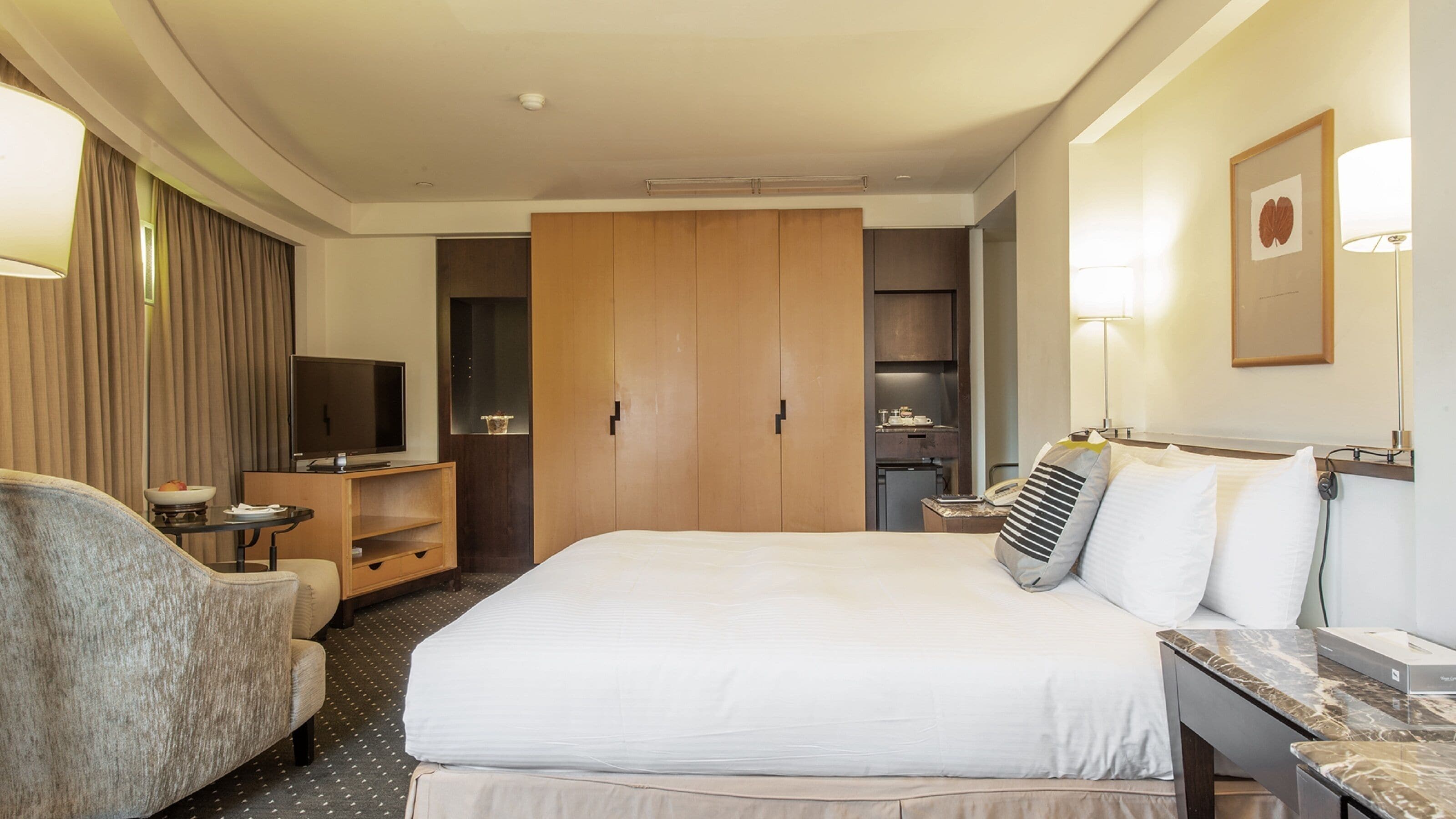A hotel room with a bed, a desk, a chair, a television, and a wardrobe.