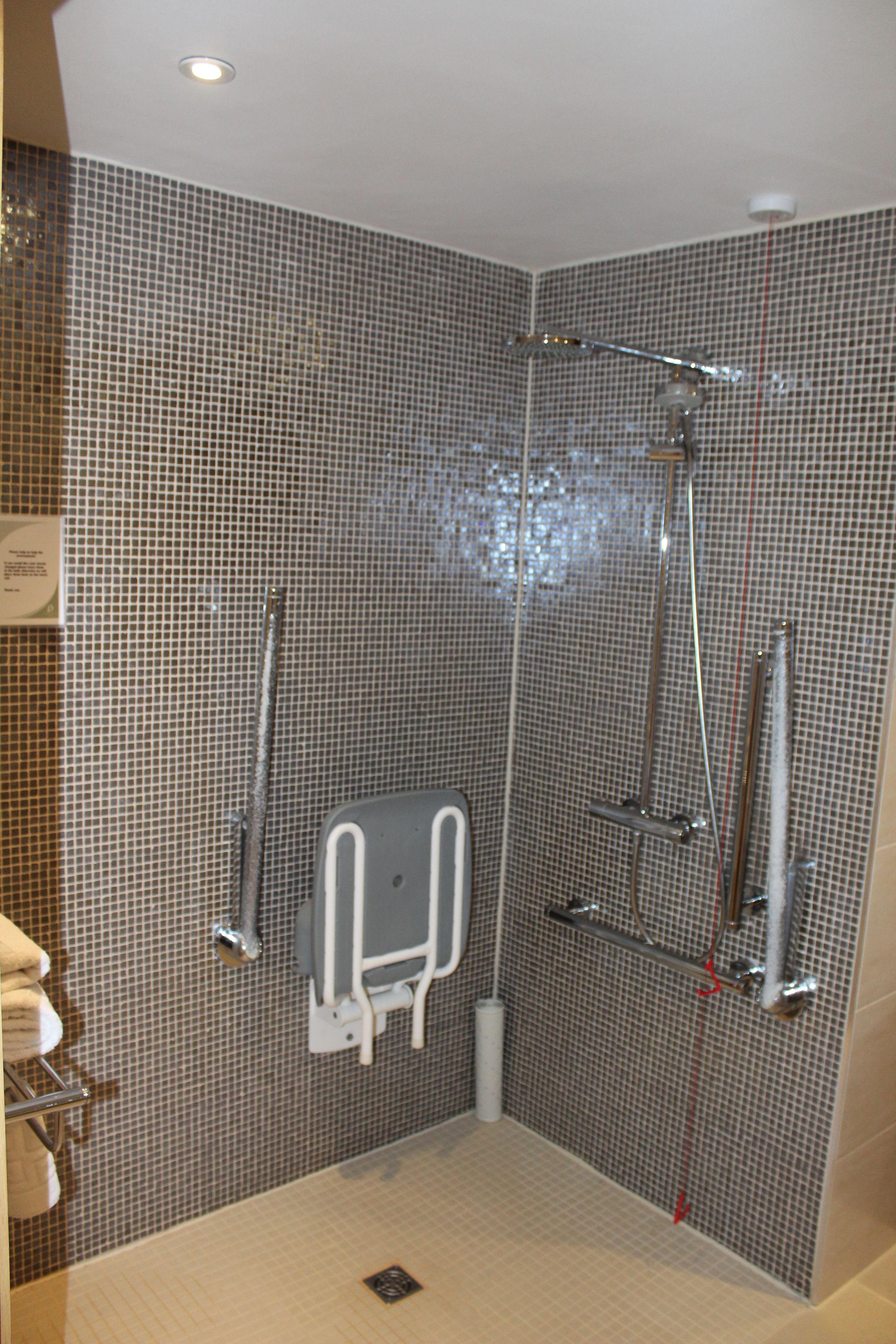 Zona de ducha con paredes de azulejos, ducha de mano, grifo empotrado en la pared y control manual de la ducha.
