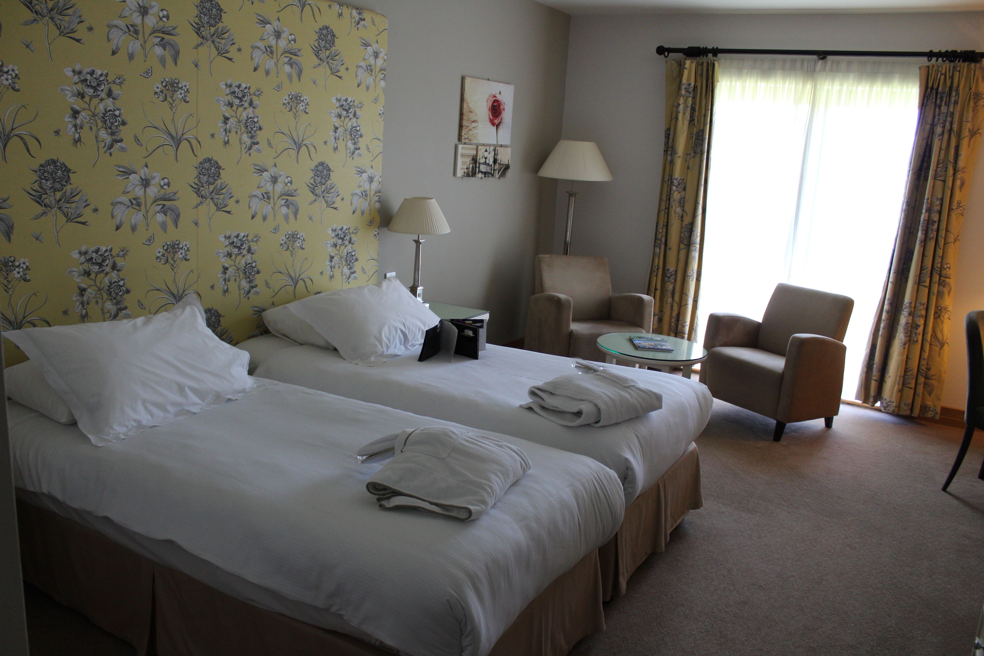 A hotel room with two beds, a chair, a table, and a lamp.