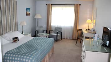 A hotel room with a bed, two chairs, a desk, a TV, and a window with curtains.