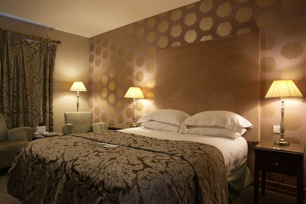 Una habitación de hotel con una cama grande, dos mesitas de noche con lámparas, una silla y una cortina.
