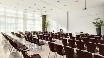 A conference room with rows of chairs, a podium, and large windows allowing natural light.