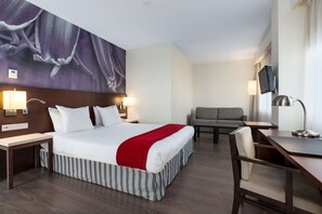 Una habitación de hotel con una cama grande, un escritorio, una silla, un sofá y un televisor montado en la pared.