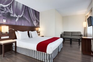 Habitación de hotel con una cama grande, un sofá, un televisor y un cuadro en la pared.