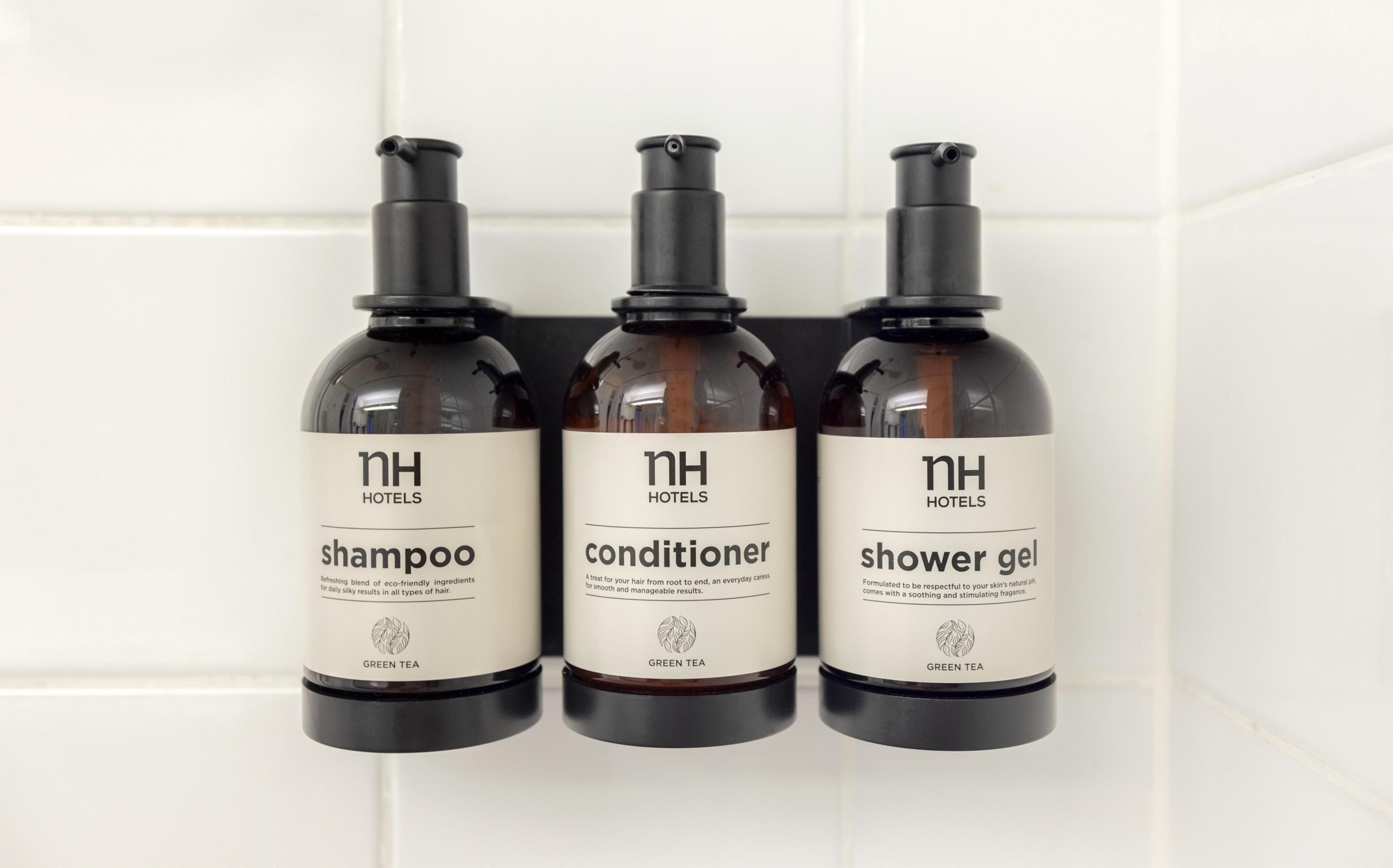 Three bottles of hotel amenities: shampoo, conditioner, and shower gel, all labeled with 'NH Hotels' and 'GREEN TEA'.