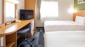 Quarto de hotel com escrivaninha, televisão, duas camas e janela com cortinas.