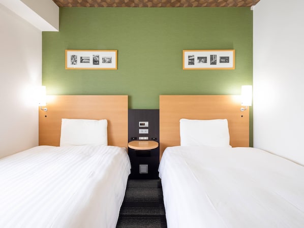 A hotel room with two beds, green walls, and framed pictures on the wall.