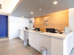 A reception desk with three computers, a wooden wall with a 'C' logo, and a blue wall. - Comfort Hotel Kurosaki (Kitakyushu)
