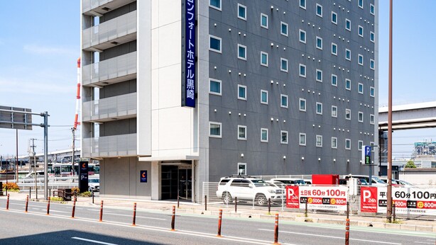 Um hotel moderno com estrutura em vários andares, uma placa de destaque com a palavra 'Comfort' e uma área de estacionamento visível com vagas demarcadas.