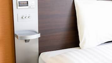 A hotel room with a bed, a bedside table with a digital clock, and a power outlet.