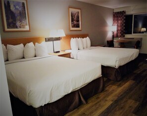 Habitación de hotel con dos camas, una mesita de noche, una lámpara y dos cuadros en la pared.