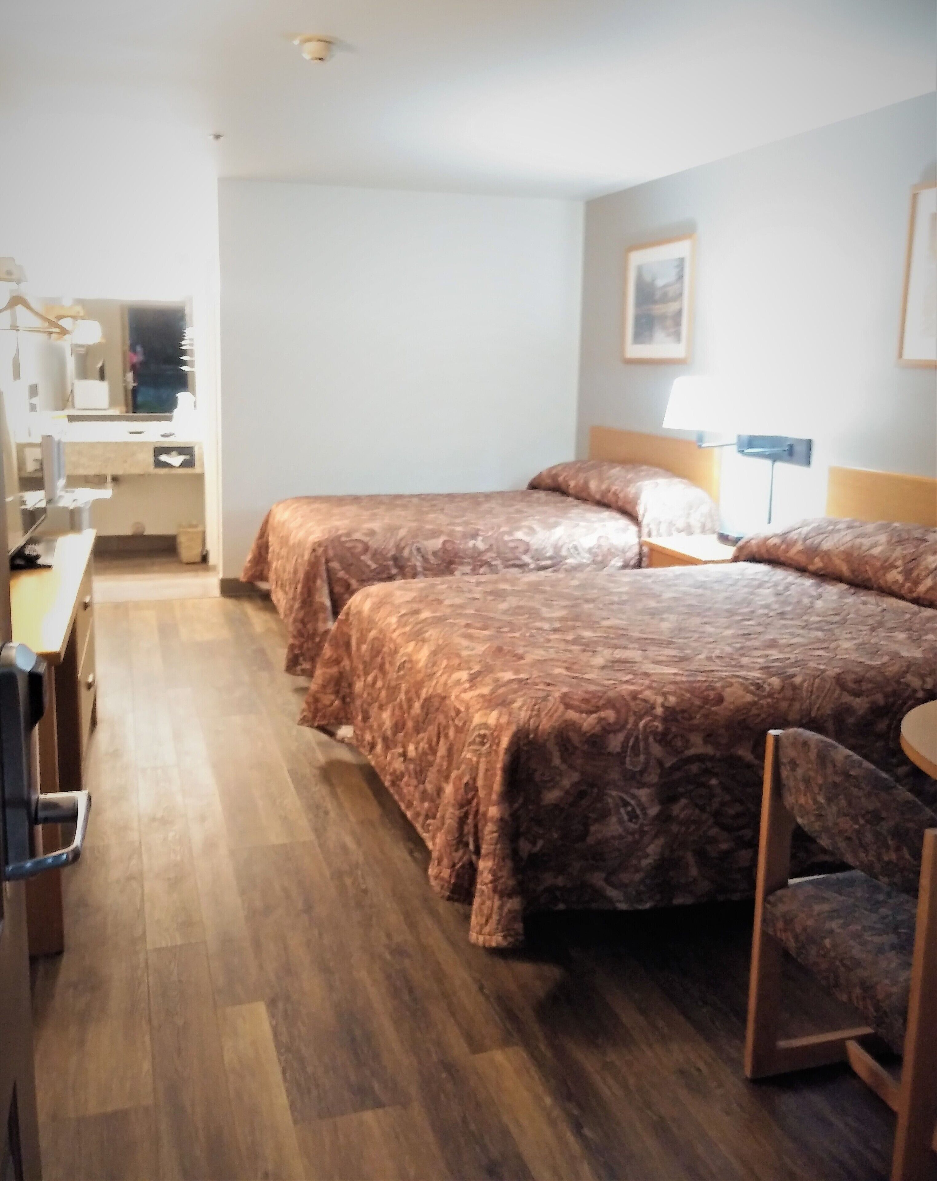 A hotel room with two beds, a desk, and a chair.