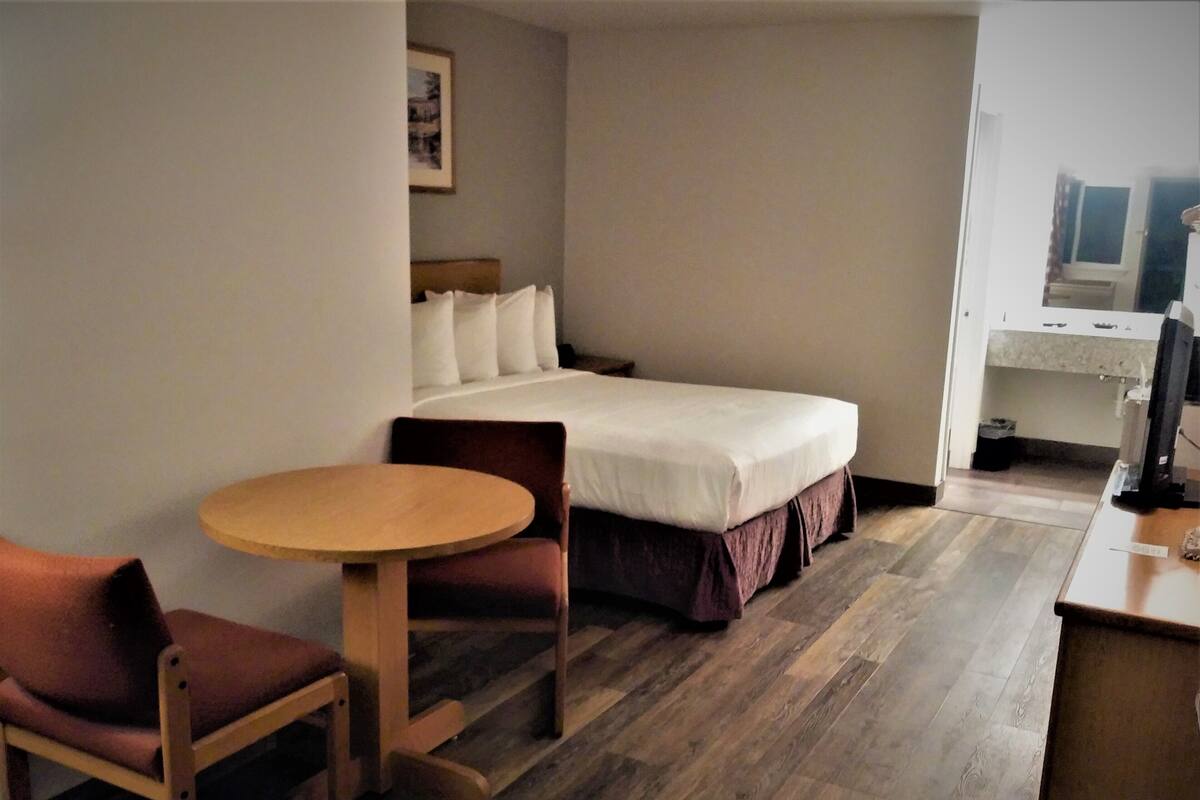 A small hotel room with a single bed, a wooden table, two chairs, and a desk with a computer.