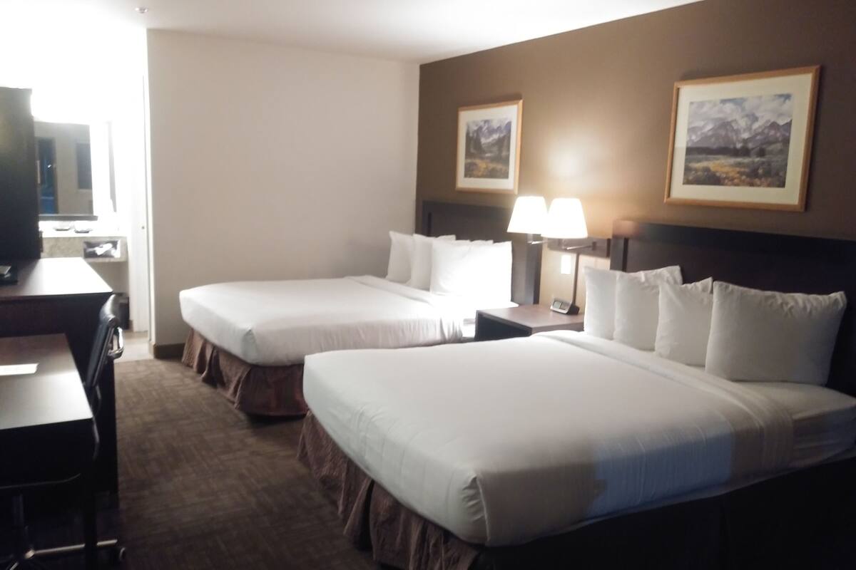 A hotel room with two beds, a desk, and a television.