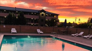 Piscina con sillones de descanso y un edificio al fondo durante el atardecer.