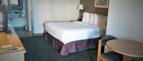 A hotel room with a bed, a desk, a chair, a lamp, and a painting on the wall.