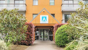 A modern building with a prominent 'A' logo, a gated entrance, and surrounding greenery.