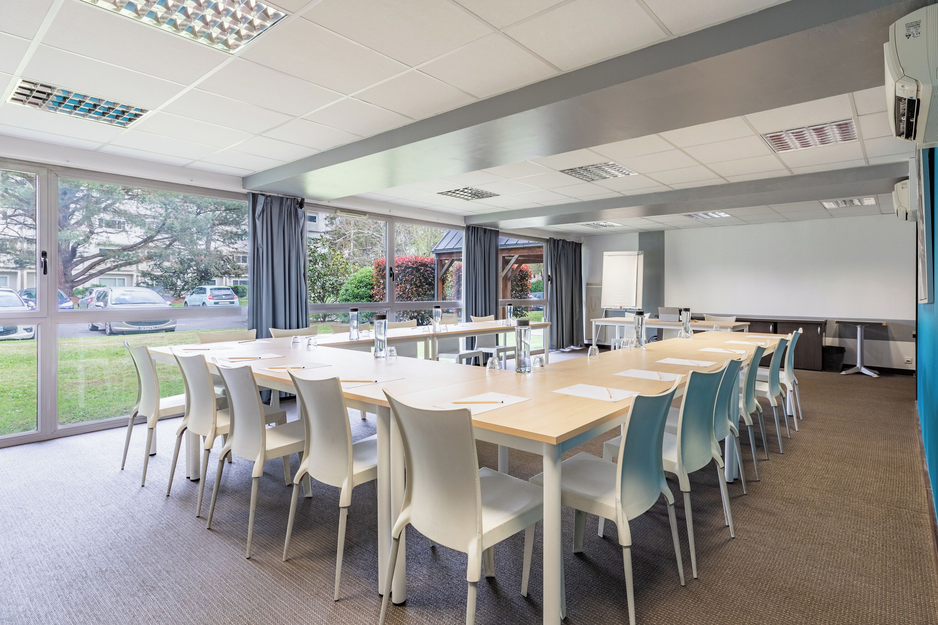 Une salle de conférence équipée d’une grande table, de chaises blanches et d’un écran de projection.